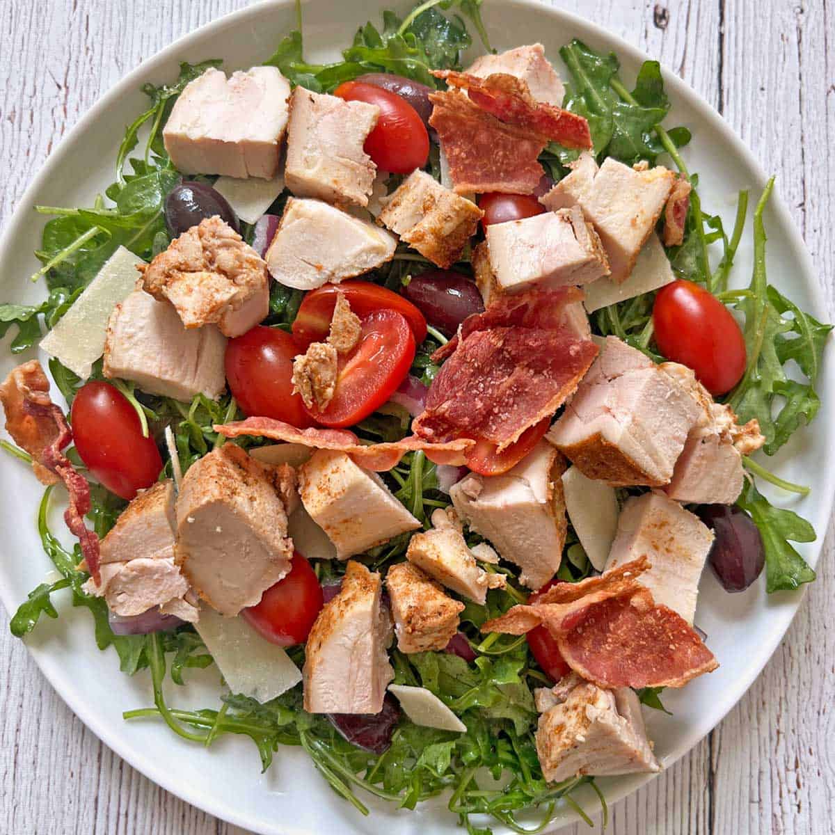 Arugula salad is topped with chicken and bacon.