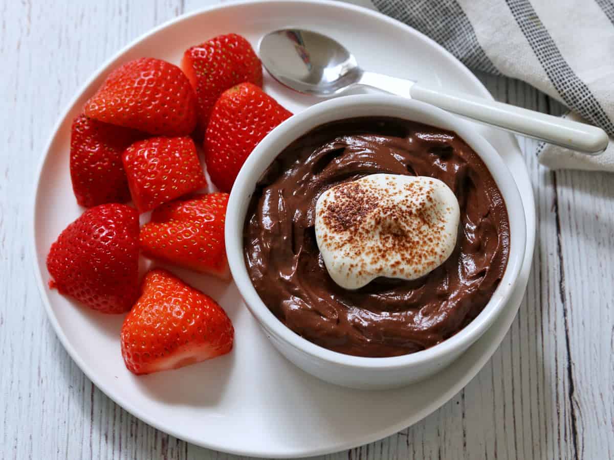 Avocado chocolate mousse is topped with whipped cream and served with strawberries.