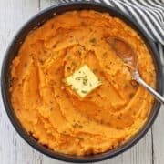 Mashed sweet potatoes are served in a dark bowl with a serving spoon.