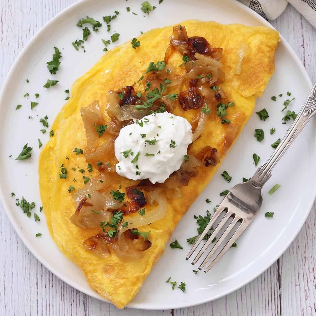 An omelette is topped with sauteed onions and sour cream.