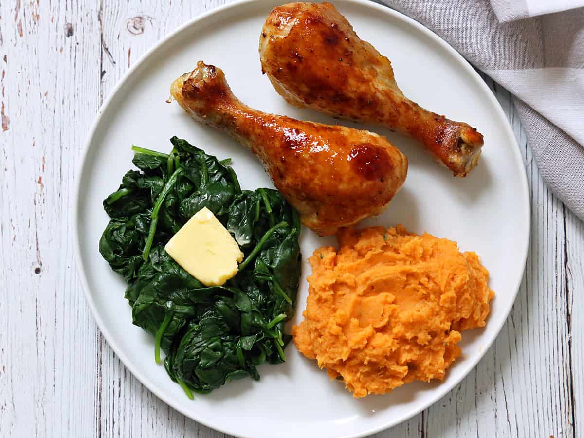 Sauteed spinach is served as a side dish to chicken along with mashed sweet potatoes.