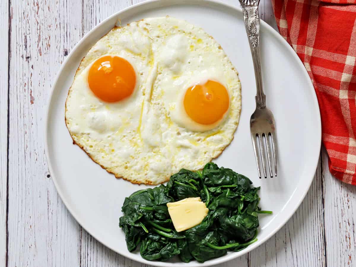 Sauteed spinach is served with fried eggs.