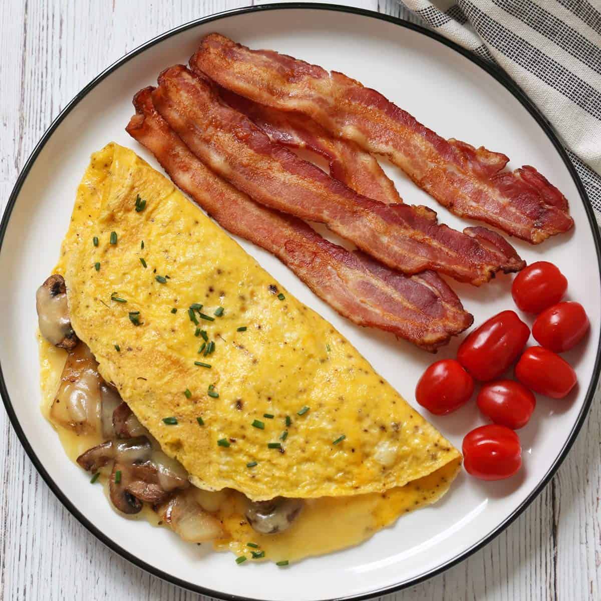 A mushroom omelette is served with bacon and tomatoes.