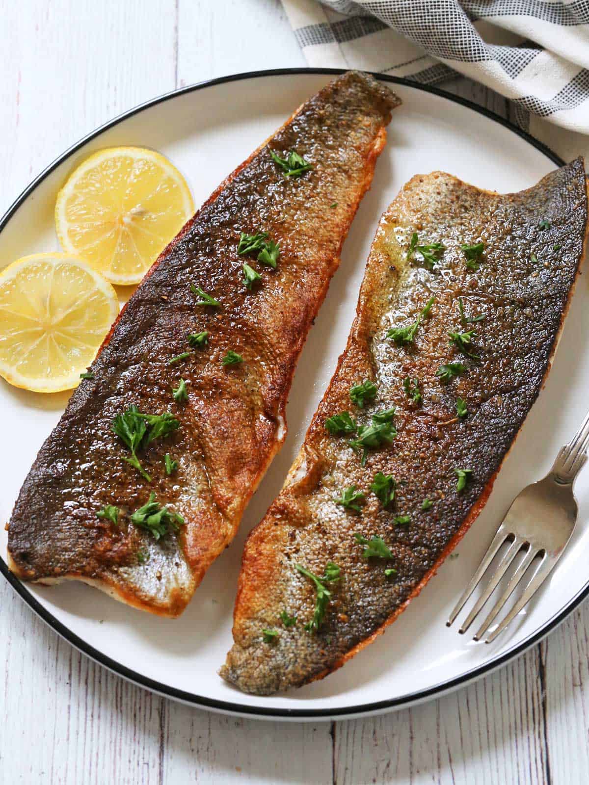 Two rainbow trout fillets are served with lemon slices.