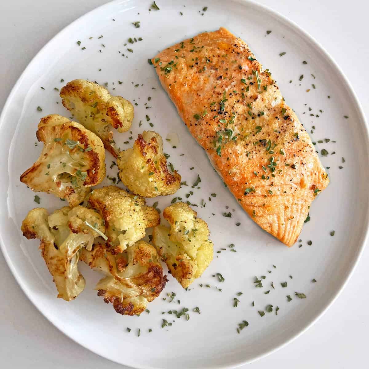 Baked salmon is served on a white plate with roasted cauliflower.