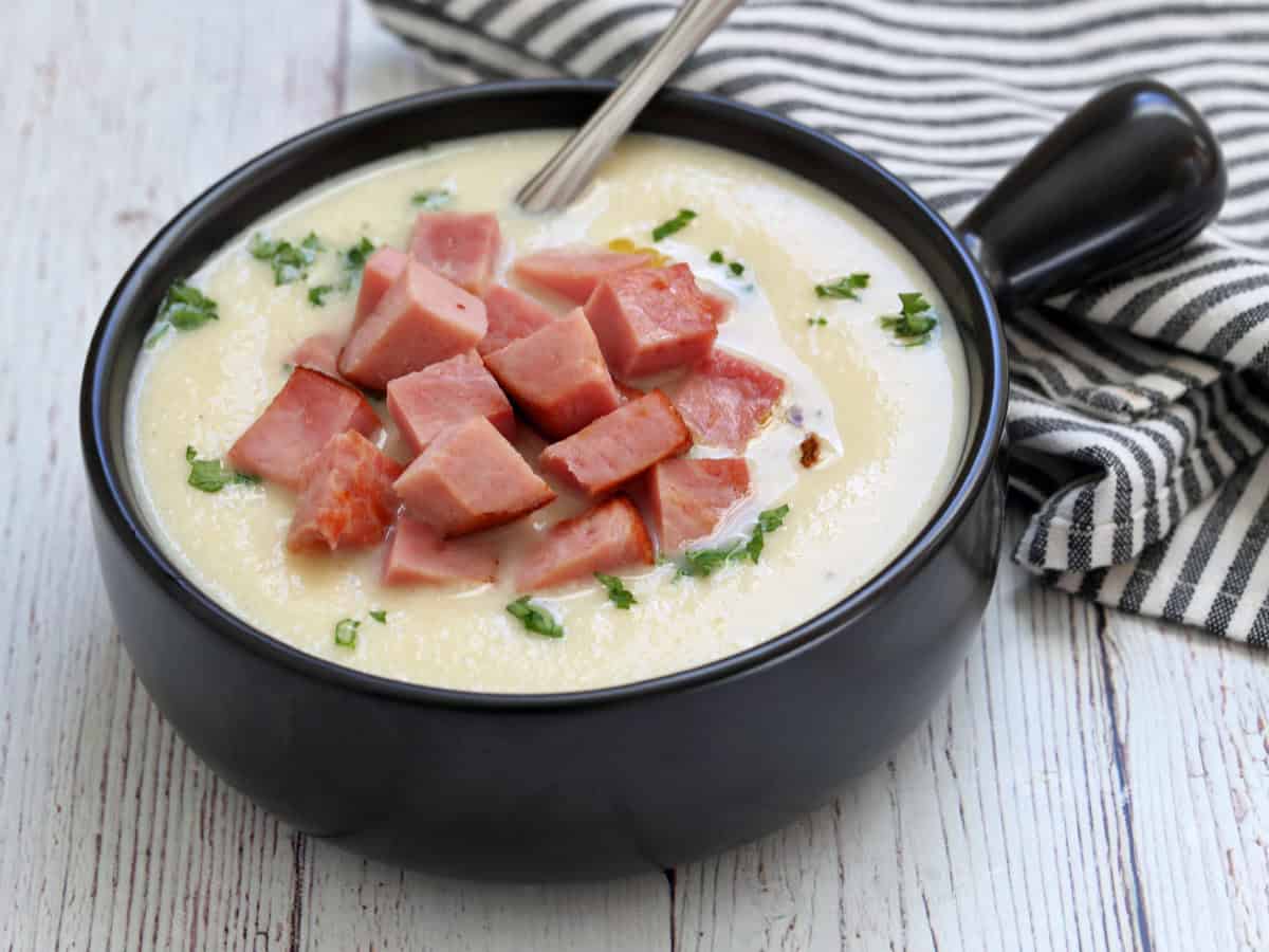 Cauliflower soup is topped with ham.