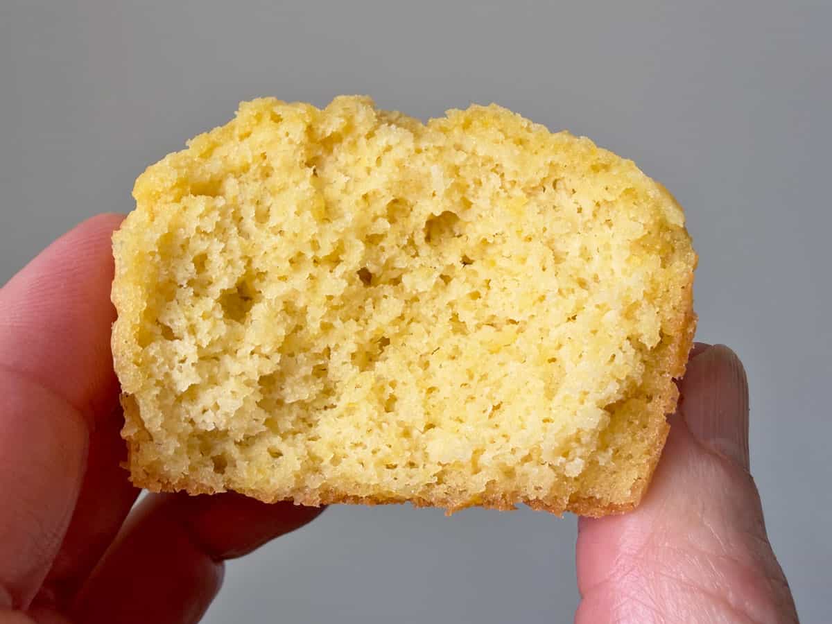 Holding a half-eaten cornbread muffin in the air to show its soft texture.