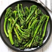 Grilled broccolini is served on a dark plate.