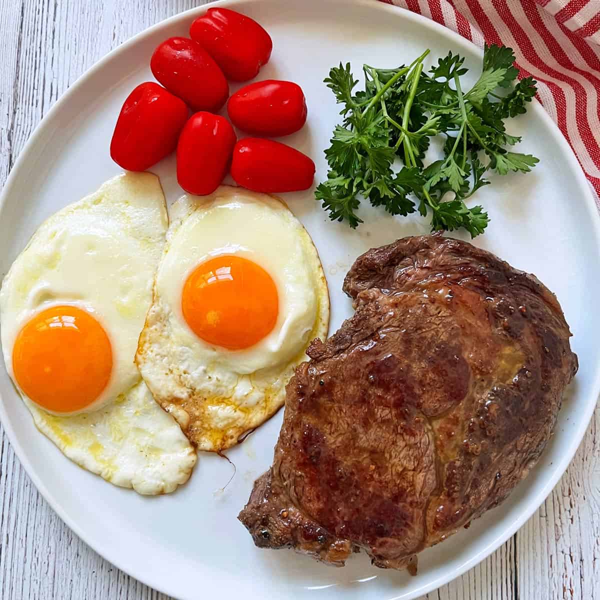 A ribeye steak is served for breakfast with fried eggs and tomatoes.