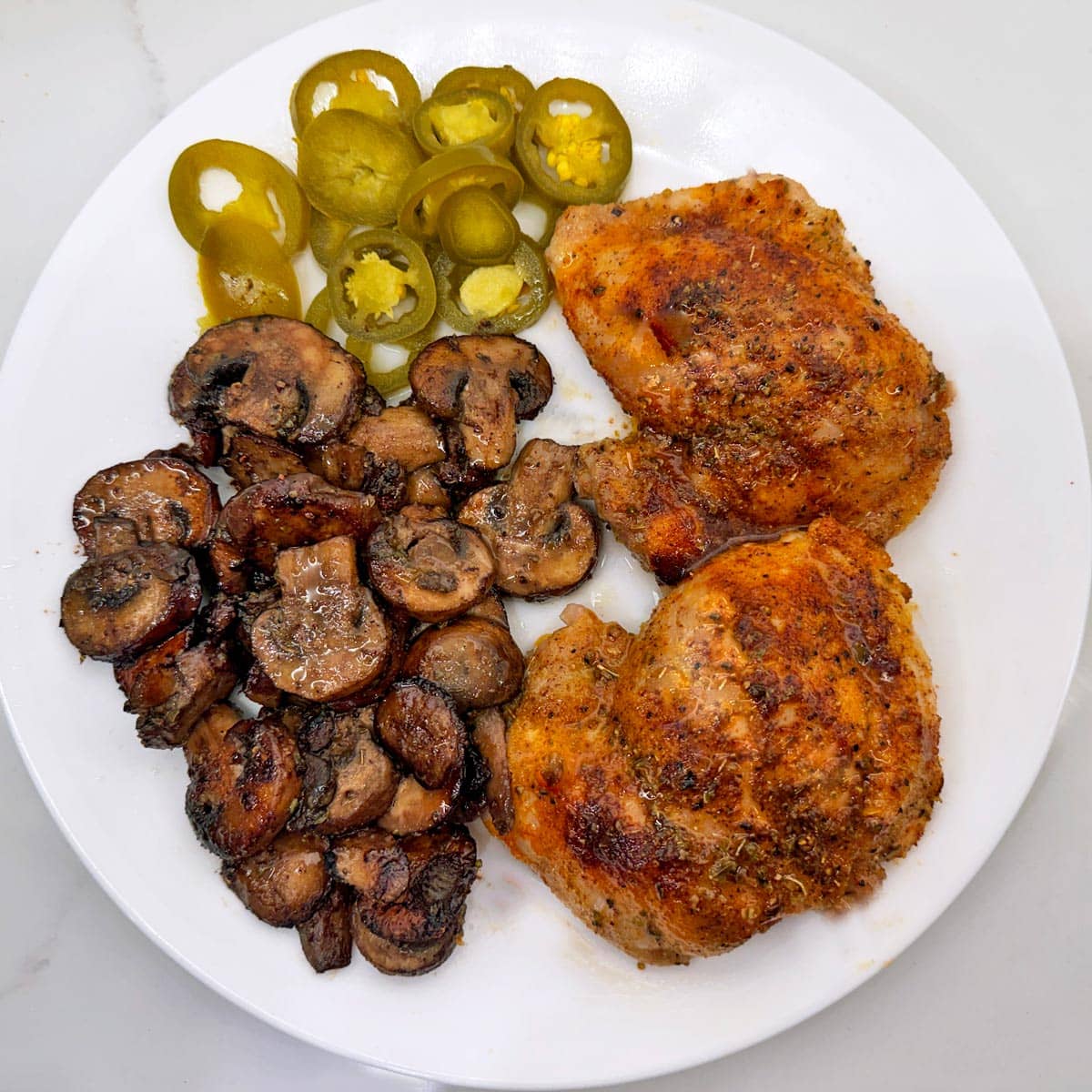 Sauteed cremini mushrooms are served with chicken thighs and pickles.