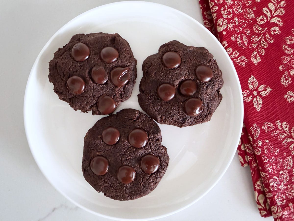 Three chocolate chocolate chip cookies on a plate.