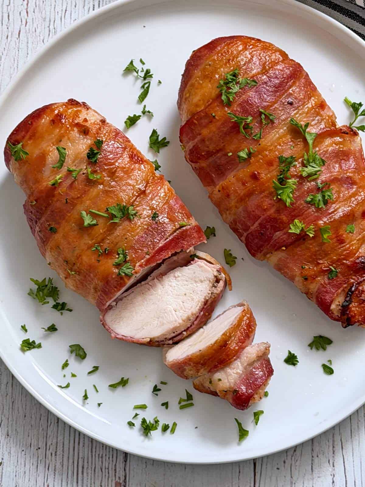 Two pieces of bacon wrapped chicken breast are served on a white plate.