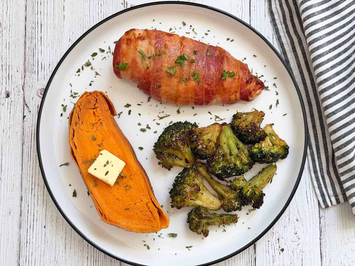 Bacon wrapped chicken breast is served with a sweet potato and broccoli.