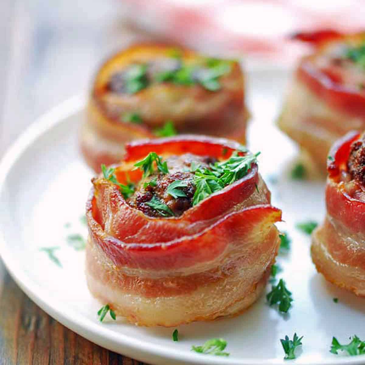 Bacon wrapped mini meatloaves are served on a white plate.