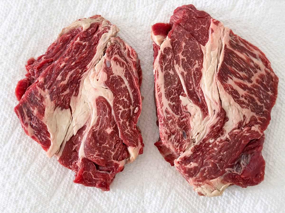 Two chuck eye steaks on paper towels.