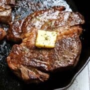 A chuck eye steak in a cast-iron skillet is topped with butter.