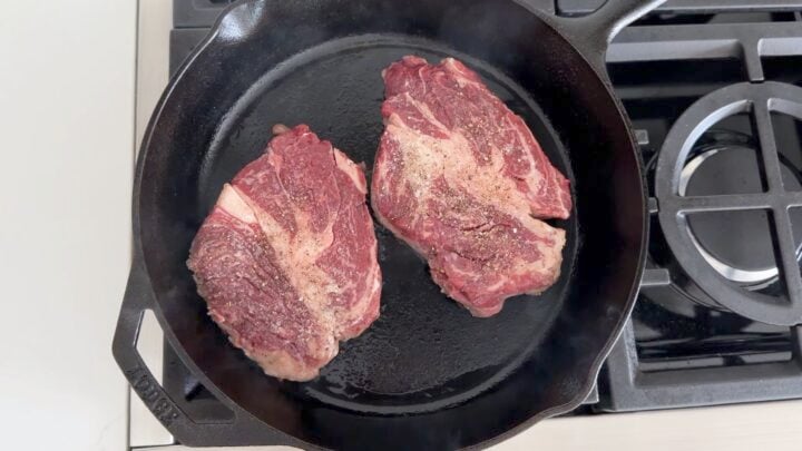 Two chuck eye steaks in a cast-iron skillet.