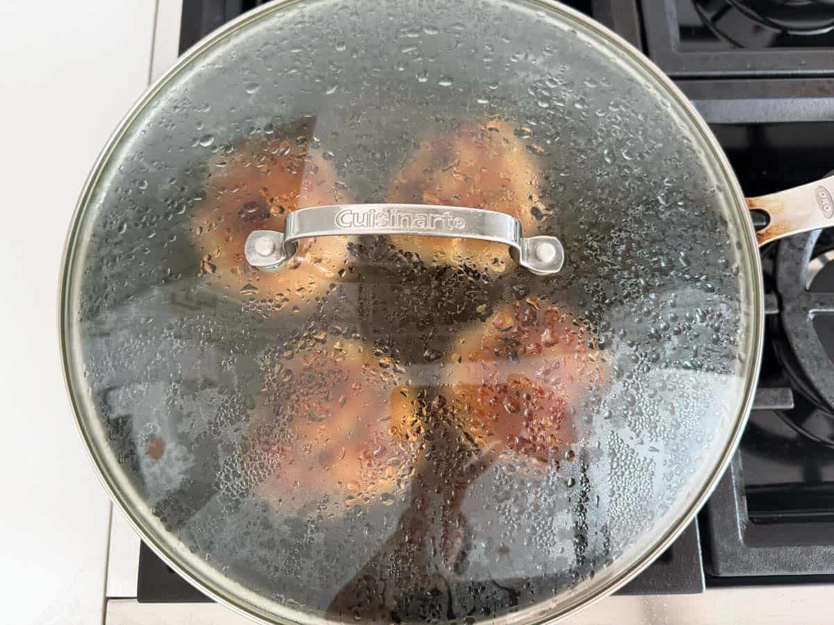 Covering the pan with a lid to finish cooking the burgers.
