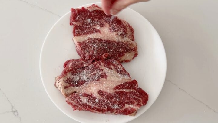 Seasoning chuck eye steaks with salt and pepper.
