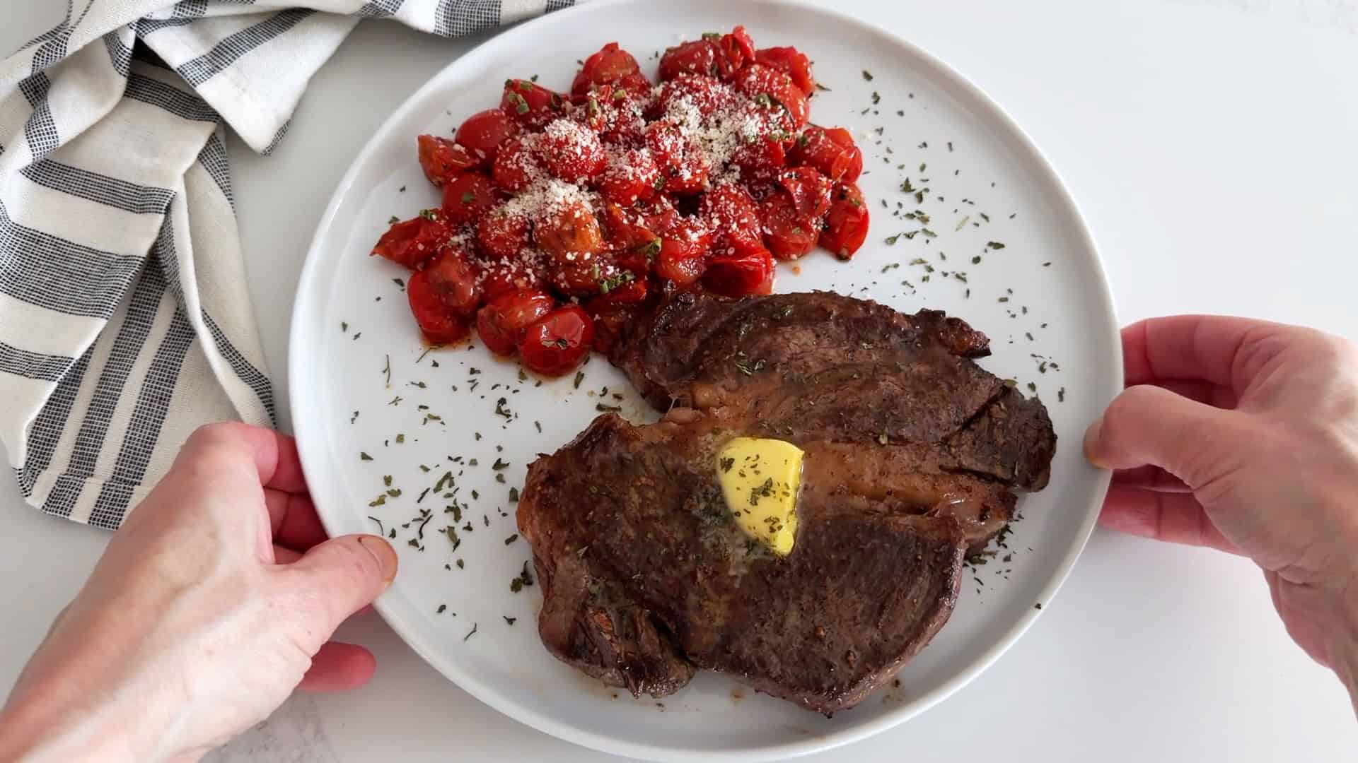 Chuck eye steak is topped with butter and served with roasted cherry tomatoes.