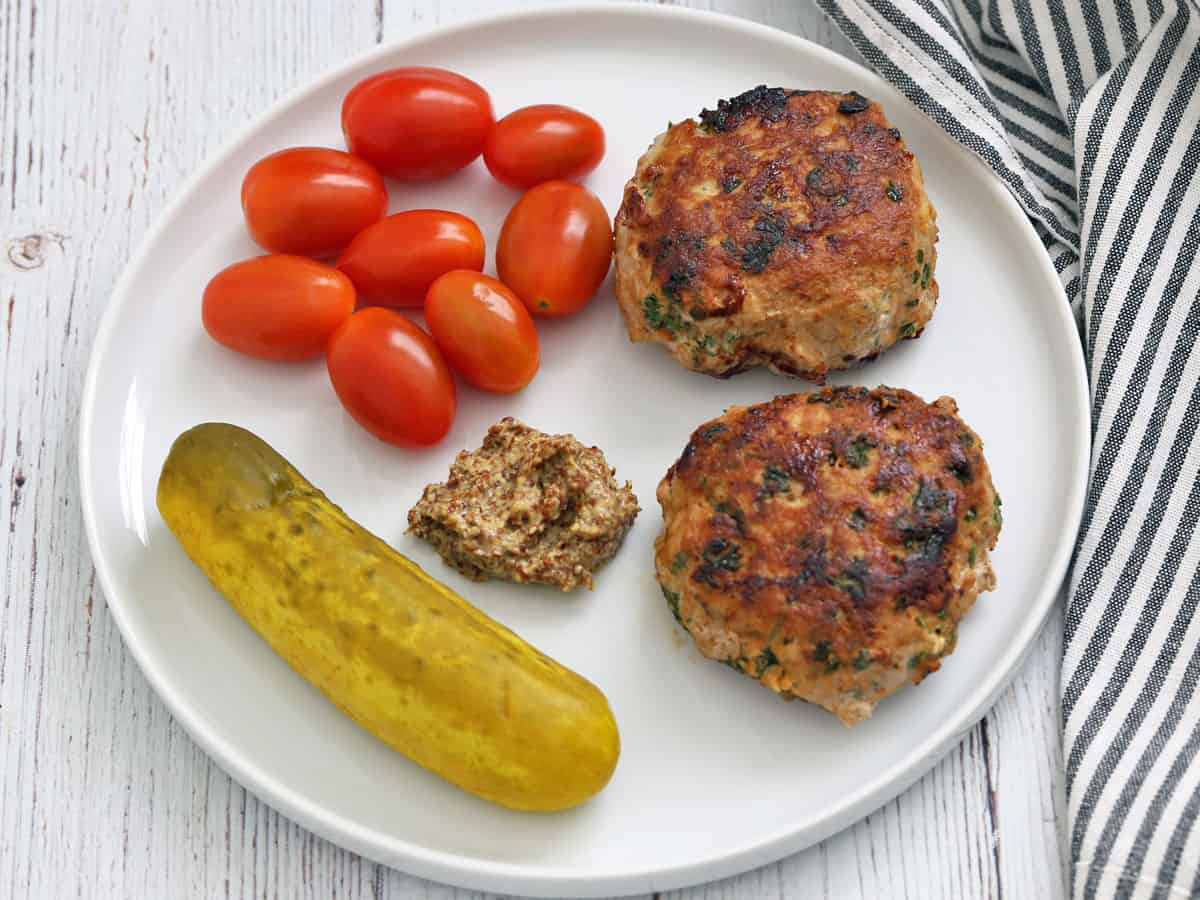 Turkey burgers leftovers are served with tomatoes, a dill pickle, and mustard.
