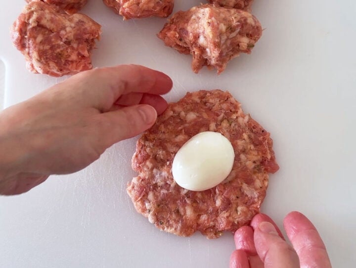 Placing an egg on top of a circle of sausage meat.