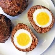 Scotch eggs are served on a white plate.