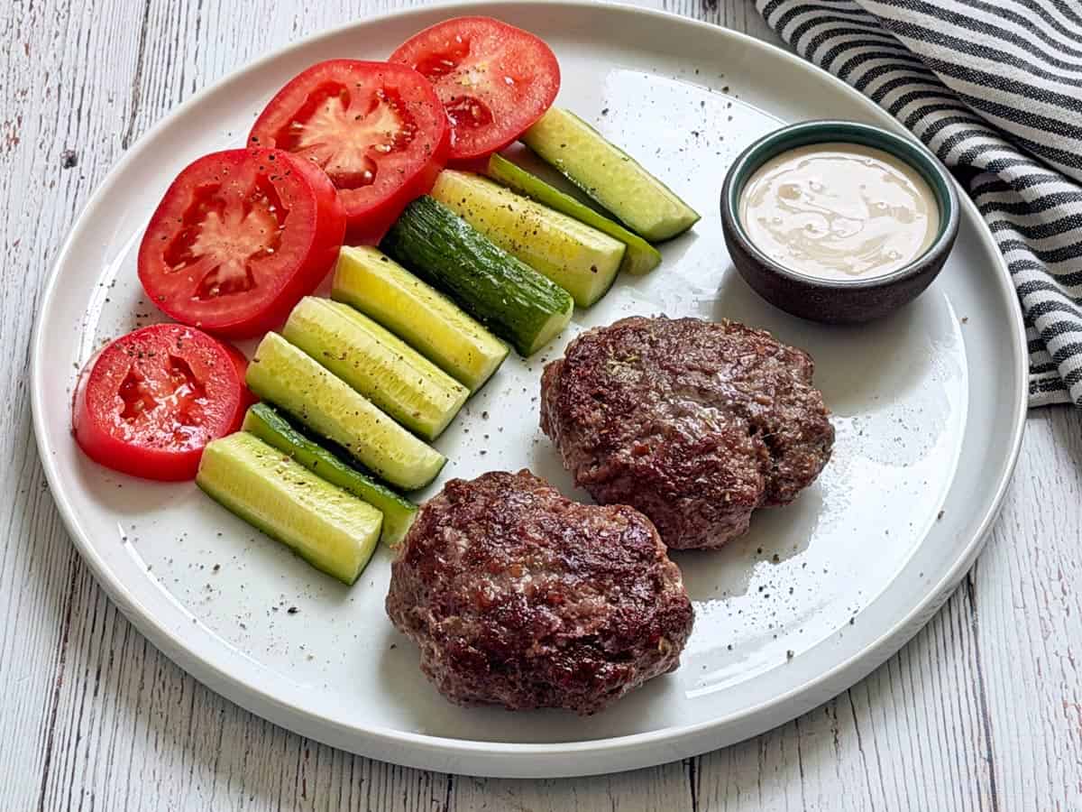 Lamb burgers leftoveres are served with cut veggies and tahini sauce.